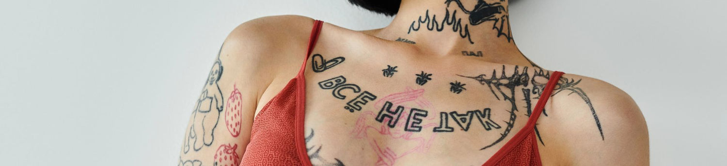 A stylish woman confidently displays her tattoos and outfit against a plain backdrop.