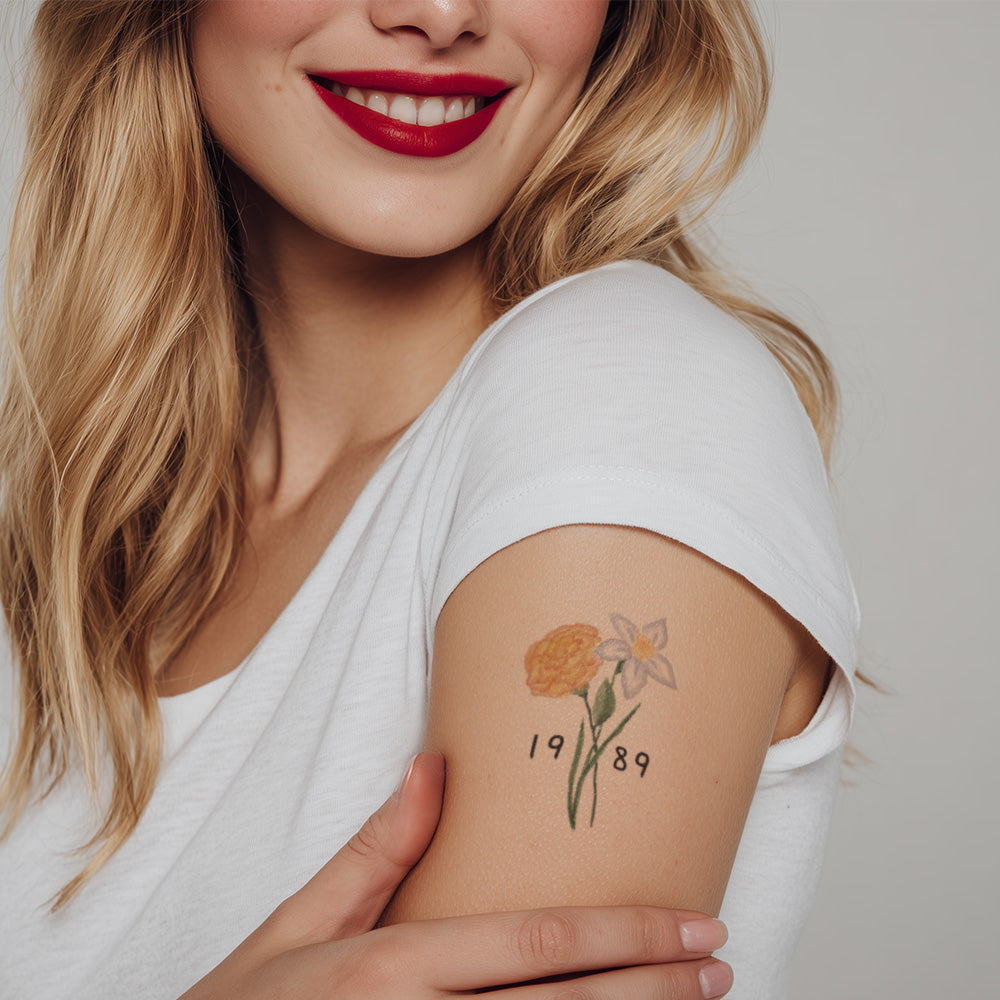 Woman with a floral tattoo on her arm wearing a white top against a neutral background