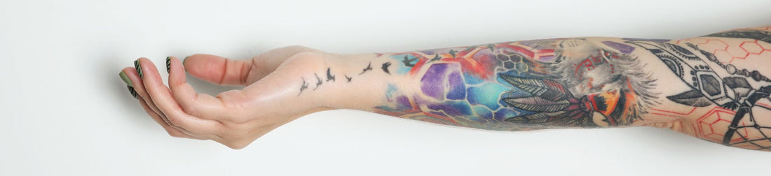 Woman with colorful tattoos on arm against white background, closeup 
