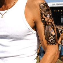 Tattoo on a person's arm with a detailed design, including a figure and text, against a blurred background.