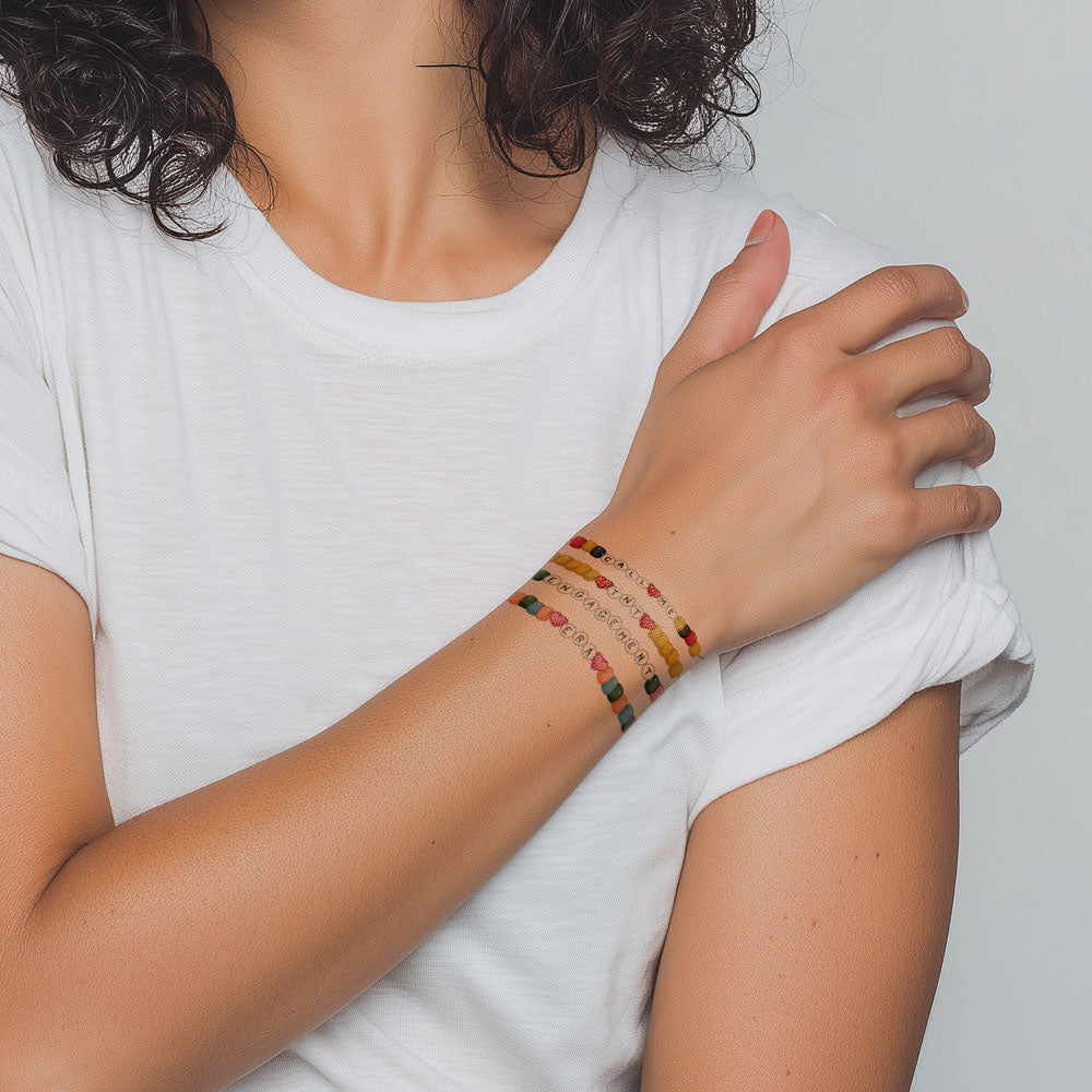 Person wearing colorful beaded tattoo bracelets on a plain background