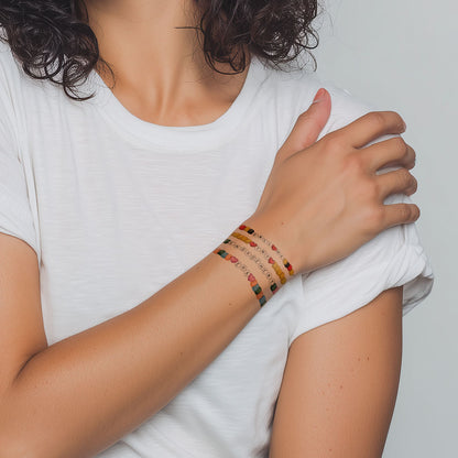 Person wearing colorful beaded tattoo bracelets on a plain background