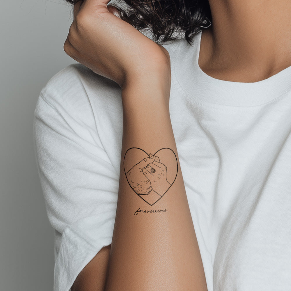 Person wearing a heart-shaped tattoo on their arm with a neutral background