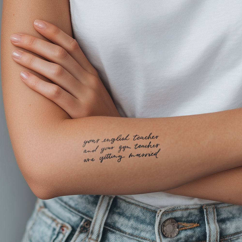 Person wearing a tattoo on their arm with text, wearing a white shirt and denim jacket.