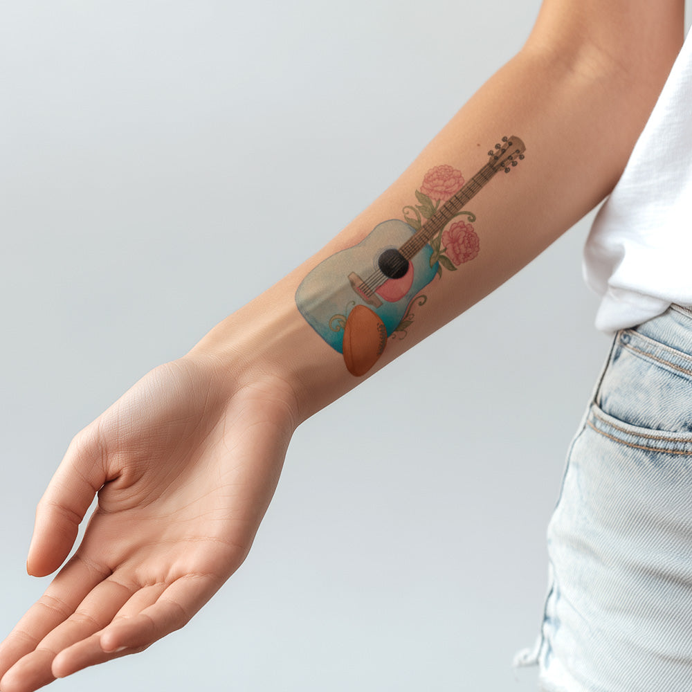 Tattoo of a guitar with flowers on a person's arm against a light gray background