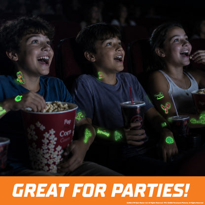 Three children sitting in a movie theater laughing and eating popcorn, with glowing green light-up sticker graphics on their clothing and drink cups. An orange banner at the bottom reads 'GREAT FOR PARTIES!'.