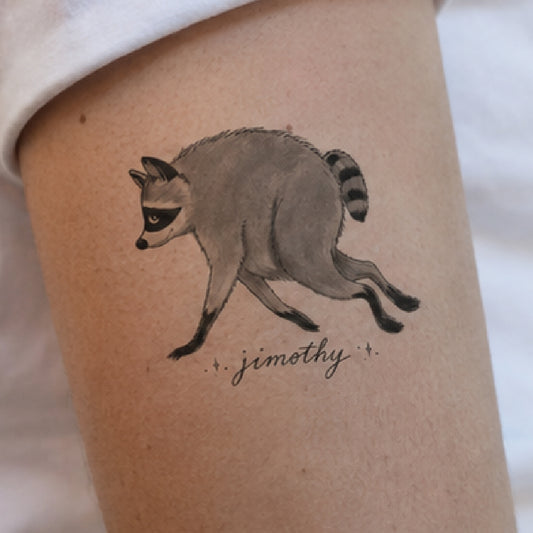 A temporary tattoo of a running raccoon with the name 'jimothy' written below in cursive, shown applied to a person's upper arm.