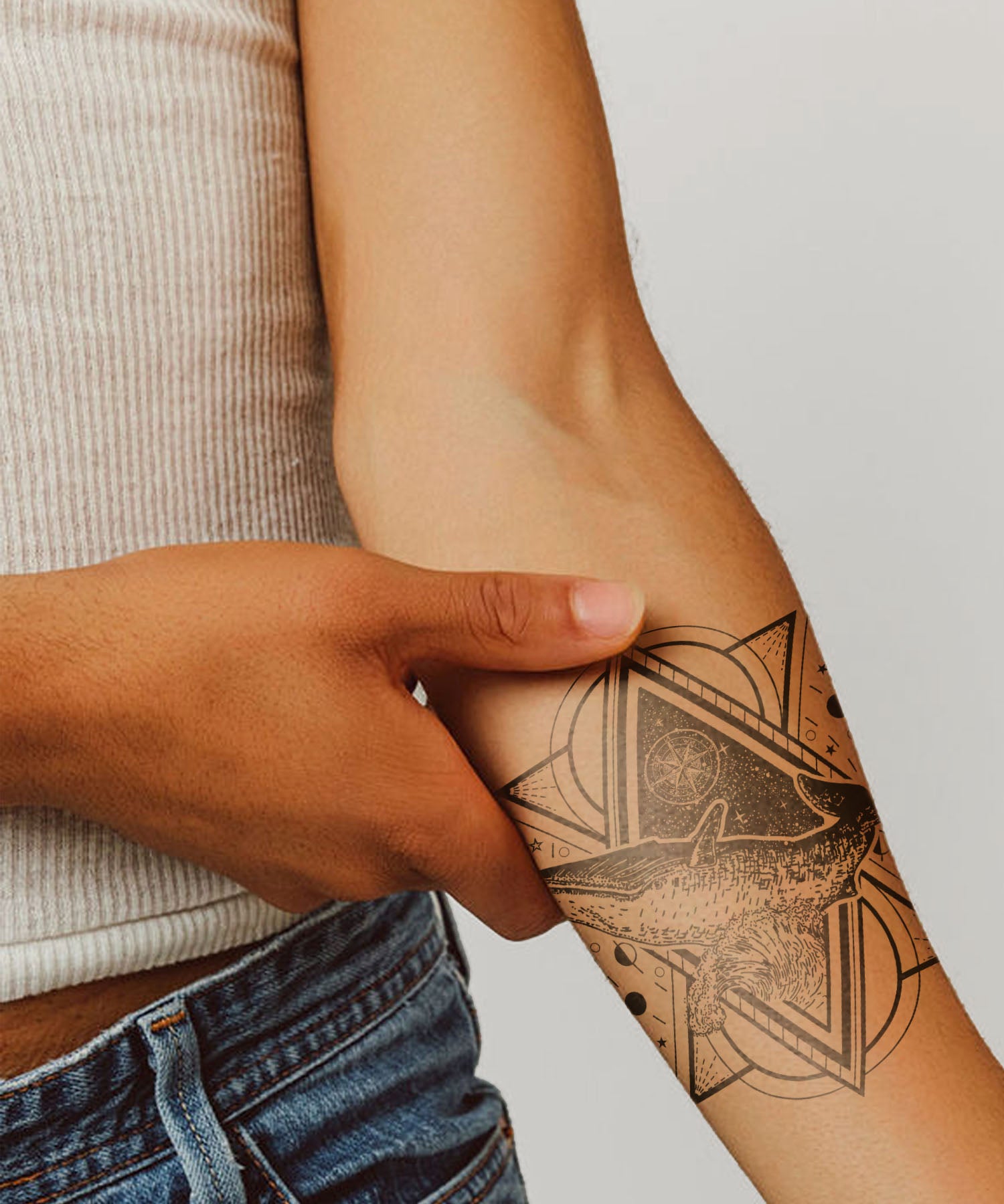 Semi-Permanent Tattoo on Person with a geometric tattoo on their arm, wearing a beige sweater and blue jeans.