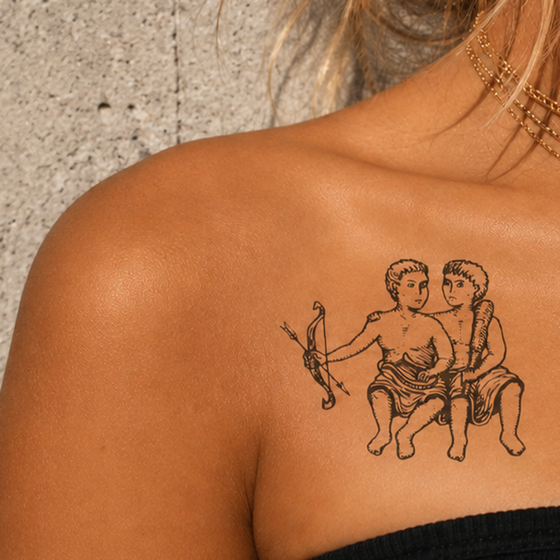 Tattoo of two figures with a bow on a person's shoulder.