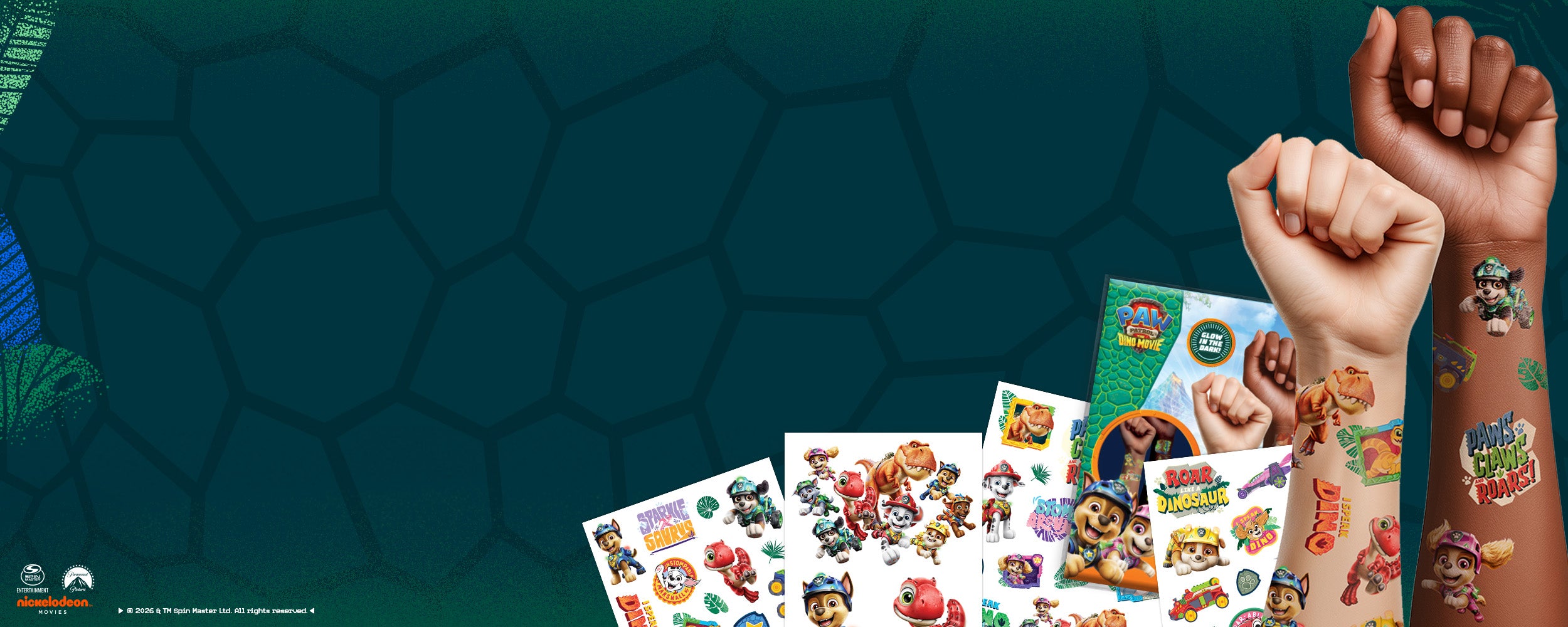 A promotional display of colorful Paw Patrol Dino Movie temporary tattoos, with two raised fists showing applied tattoo designs on the right side against a dark teal patterned background.