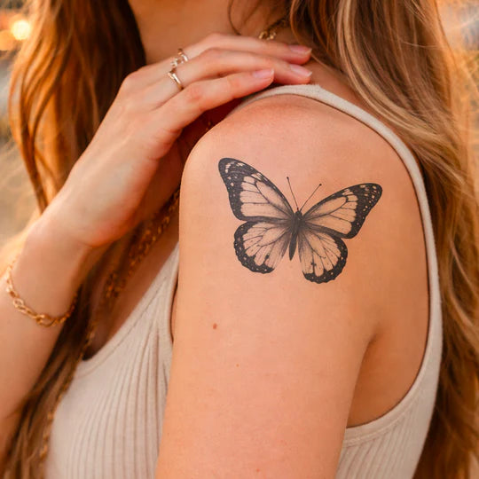 Woman with a butterfly tattoo on her arm, wearing a white sleeveless top.